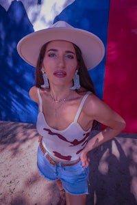 a woman in a hat and denim standing in front of a texas flag